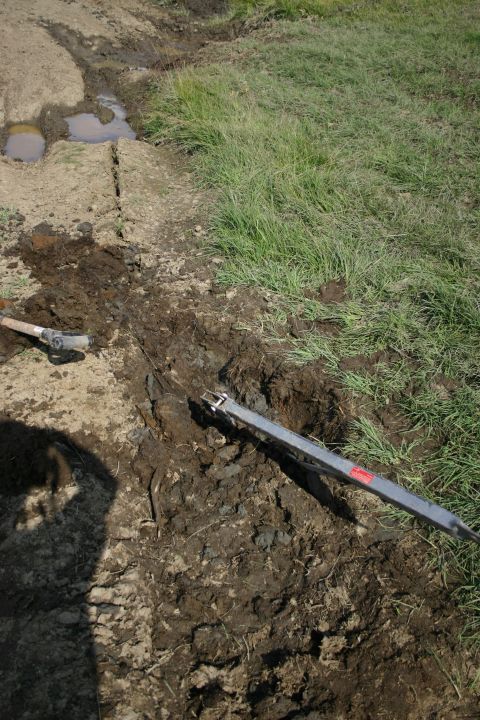 2003 Jeep TJ - Digging a trench in muddy ground with a shovel and a metal bar.