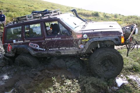 2003 Jeep TJ - This maroon Jeep Cherokee XJ is stuck deep in mud, equipped with a snorkel and roof rack for off-road adventures.