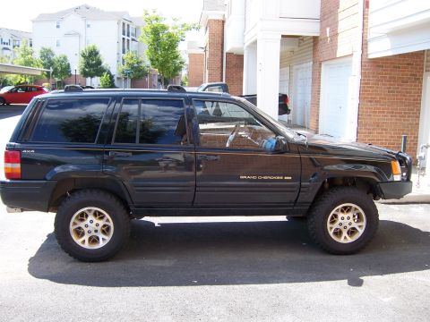 1996 Jeep Grand Cherokee - Side profile of a black 1996 Jeep Grand Cherokee with gold rims.