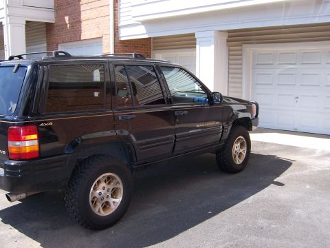 1996 Jeep Grand Cherokee - The side profile of a black Jeep Grand Cherokee shows its 4x4 badging and gold-colored wheels.