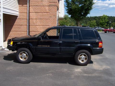 1996 Jeep Grand Cherokee - A black 1996 Jeep Grand Cherokee is parked outside a brick building, showing its lifted stance and aftermarket wheels.