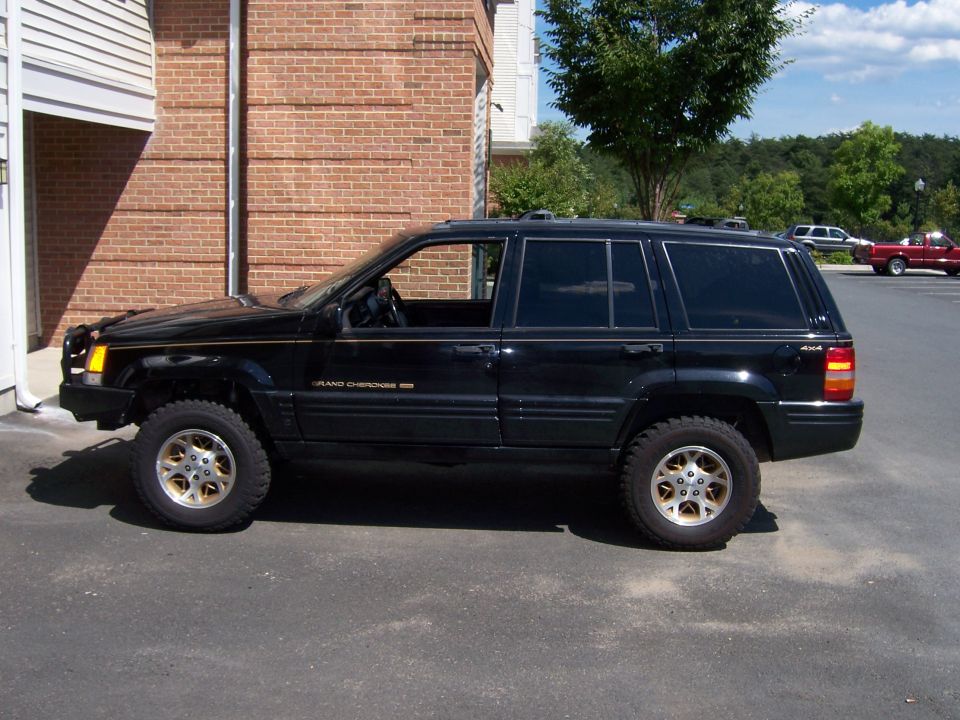 Black 1996 Jeep Grand Cherokee side view, lifted with aftermarket wheels, parked next to brick building
