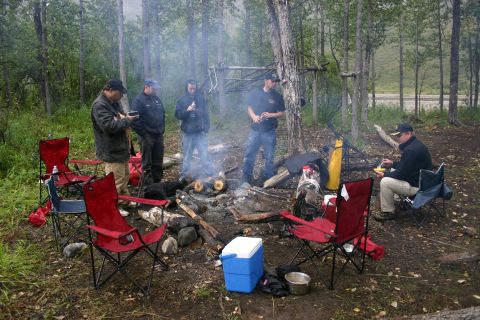 2003 Jeep TJ - A group of people enjoy a campfire in a forest clearing, with chairs set up around the fire pit.