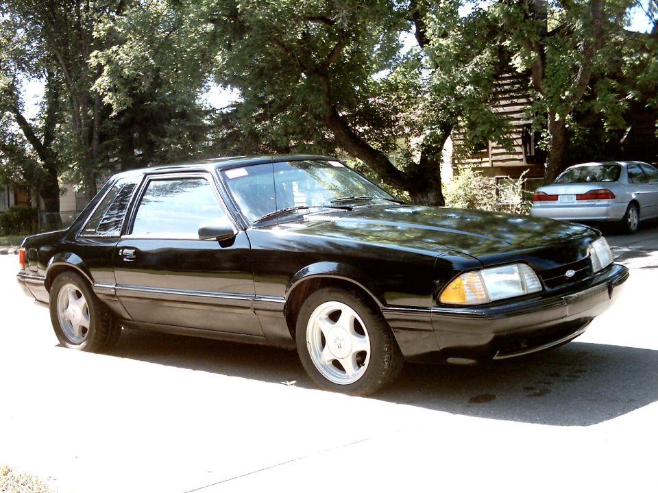 Black Fox-body Mustang notchback coupe on Pony wheels, front three-quarter view on a residential street