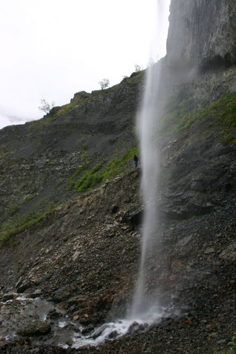 2003 Jeep TJ - A lone figure stands on a rocky outcrop beside a tall waterfall, observing the natural landscape.