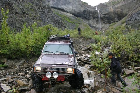2003 Jeep TJ - Maroon Jeep Cherokee XJ navigates rocky terrain with a waterfall in the background.