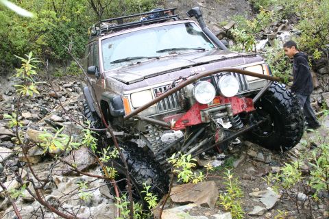 2003 Jeep TJ - Modified Jeep Cherokee XJ tackling a challenging off-road trail with large tires and a winch.