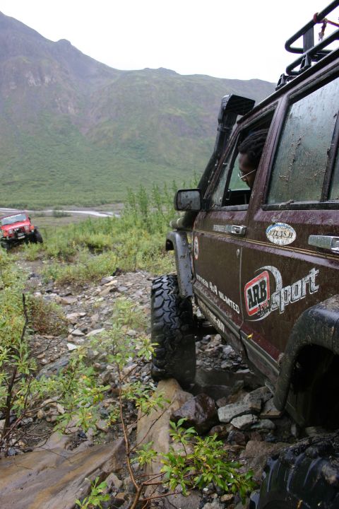 2003 Jeep TJ - Two off-road vehicles navigate a challenging rocky path with a mountainous landscape in the distance.