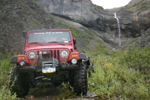 2003 Jeep TJ - A red 2003 Jeep TJ navigates a rocky, off-road path with a waterfall cascading in the background.