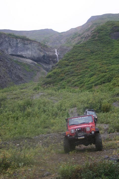 2003 Jeep TJ - Two Jeep Wranglers navigate a rocky trail leading to a waterfall in a mountainous, vegetated landscape.