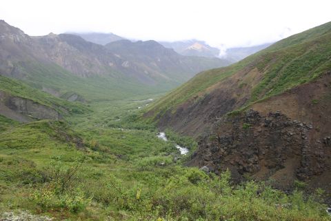 2003 Jeep TJ - A vast mountain valley landscape with a river flowing through the lush green terrain, under an overcast sky.