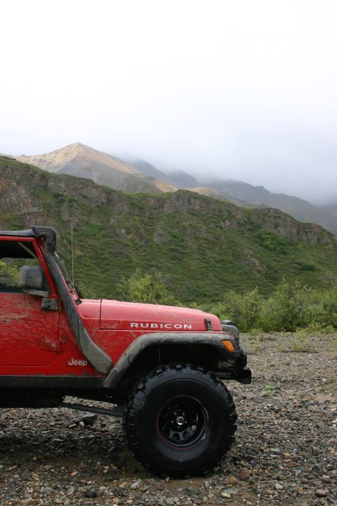 2003 Jeep TJ - Red 2003 Jeep TJ Rubicon equipped with a snorkel and off-road tires sits in a mountainous landscape.