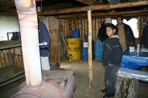 2003 Jeep TJ - A group of people are gathered inside a rustic cabin, with a wood stove and storage barrels visible.