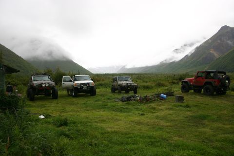 2003 Jeep TJ - Several off-road vehicles are parked in a wide, grassy valley under a cloudy sky.