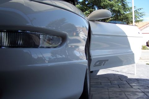 1997 Ford Probe - Close-up of a white sports car's front fender and open door, revealing a GT emblem.