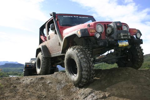 2003 Jeep TJ - A red Jeep Wrangler navigates an off-road trail with a scenic mountain landscape in the background.