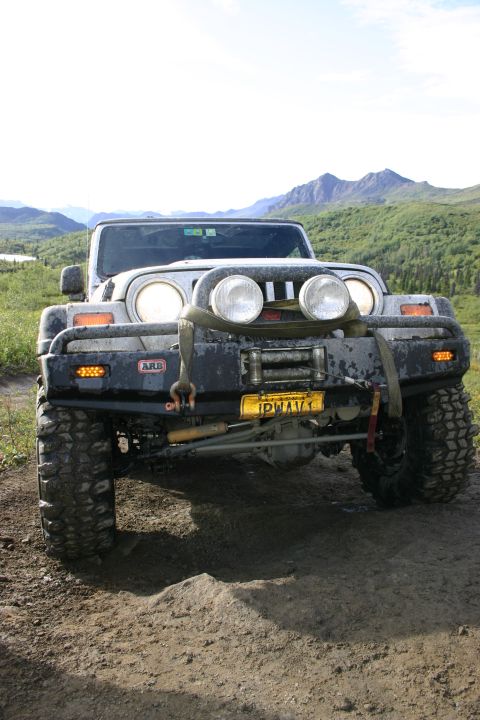 2003 Jeep TJ - Front view of a modified 2003 Jeep TJ with aftermarket bumper and winch, parked on a dirt track.