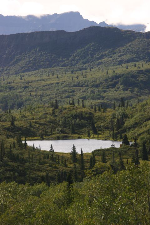 2003 Jeep TJ - A mountain landscape a calm lake reflecting the sky, with lush green forests and distant peaks.