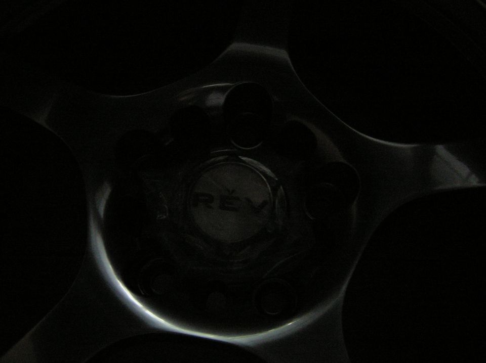 Dimly lit five-spoke alloy wheel center with REV branded center cap and lug holes
