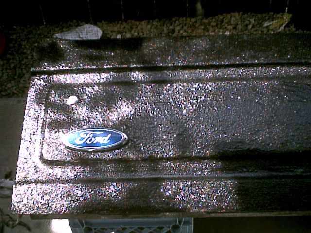 Truck panel coated in glittery metallic textured paint with a blue Ford oval emblem on gravel