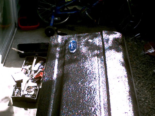 Glittery metal-flake coated tailgate with chrome Ford oval lying on the floor near an open toolbox