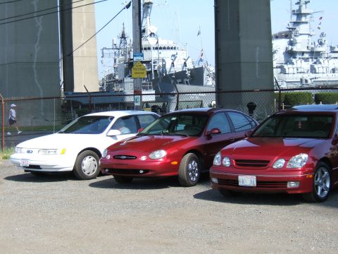 1998 Ford Taurus - Three sedans are parked in a lot with a ship in the background.