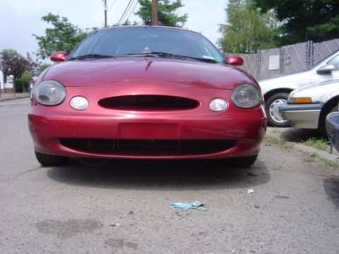 1998 Ford Taurus - A red 1998 Ford Taurus is parked on a street with another vehicle beside it.