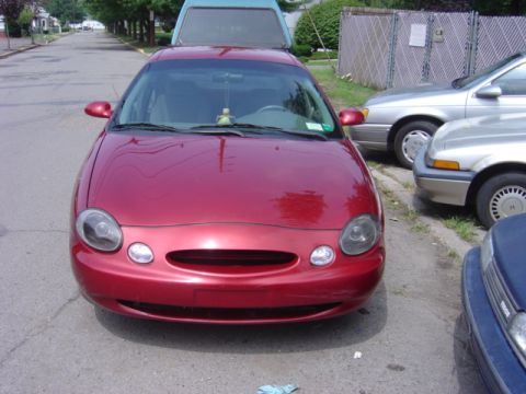 1998 Ford Taurus - A red 1998 Ford Taurus is parked on a residential street, with other vehicles visible.