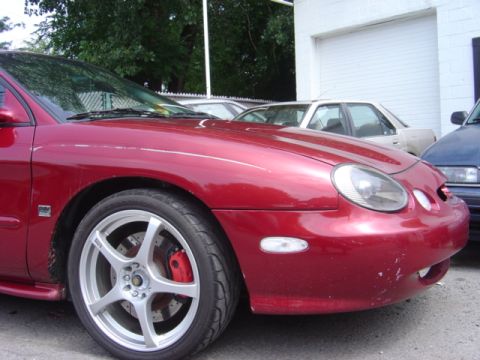 1998 Ford Taurus - Front quarter view of a red 1998 Ford Taurus, custom silver rims and visible red brake calipers.