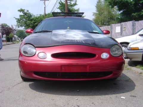 1998 Ford Taurus - Front view of a red sedan with a custom painted hood, parked outdoors next to another vehicle.