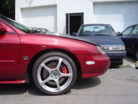 1998 Ford Taurus - A red car's front quarter panel and custom wheels are visible, with other vehicles in the background.