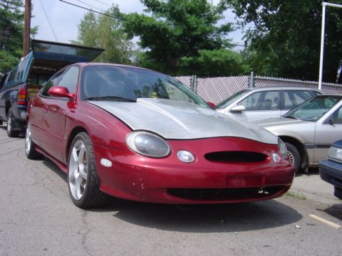 1998 Ford Taurus - Red 1998 Ford Taurus with a custom silver hood is parked outdoors.