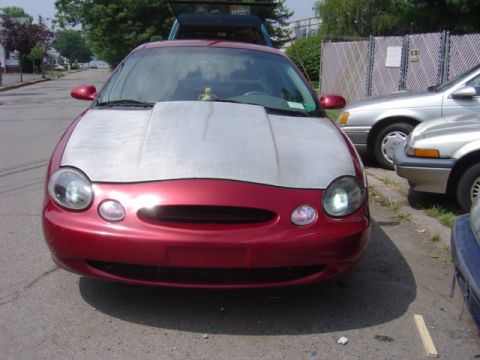 1998 Ford Taurus - A red sedan with a modified silver hood is parked on a street, with other vehicles nearby.