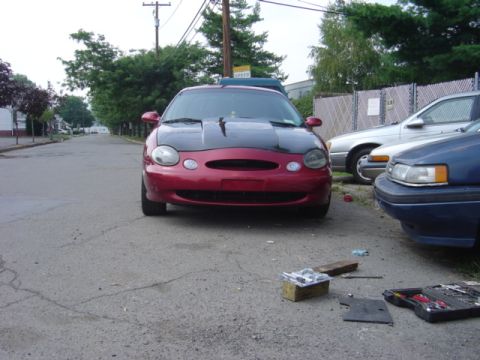 1998 Ford Taurus - This 1998 Ford Taurus is parked on a street with a black hood and red body.