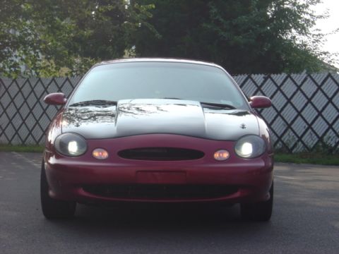 1998 Ford Taurus - Front view of a red 1998 Ford Taurus with a custom hood scoop and dark tinted headlights.