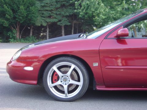 1998 Ford Taurus - A red 1998 Ford Taurus sedan is shown from the front quarter angle, aftermarket wheels and a contrasting black hood.