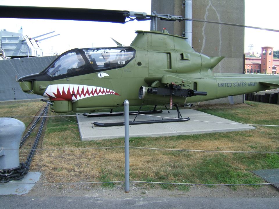 Green AH-1 Cobra helicopter with shark mouth nose art and "UNITED STATES ARMY" on tail