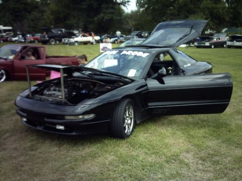 1995 Ford Probe - A black coupe is displayed with its hood and driver's door open, parked on grass at an outdoor event.