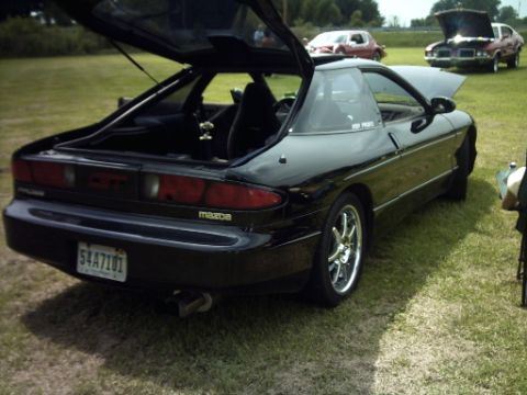 1995 Ford Probe - This black Mazda Probe is seen from the rear with its trunk and hood open, parked on a grassy field with other vehicles in the background.