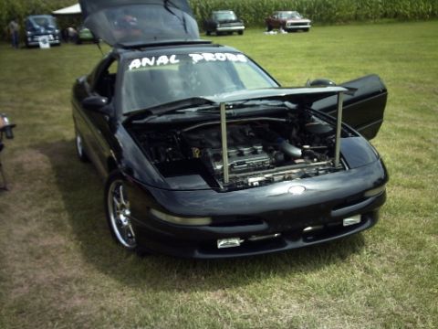 1995 Ford Probe - A black sports coupe is parked on a grassy field with its hood and trunk open, revealing the engine.