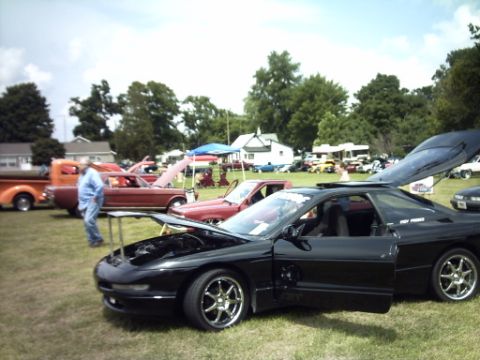 1995 Ford Probe - A black sports car is displayed with its doors and hood open at a car show, with other vehicles and attendees around.