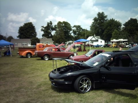 1995 Ford Probe - A black sports car is parked on the grass with its hood and door open, alongside other vehicles at an outdoor gathering.