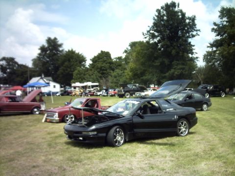 1995 Ford Probe - Several cars are parked on a grassy field under a partly cloudy sky.