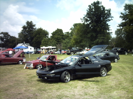 Black 1995 Ford Probe with hood open parked on grass at a car show