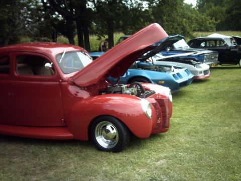 1995 Ford Probe - Several classic cars are lined up on a grassy field, with the hood of the front red coupe open.