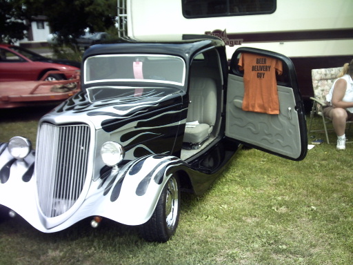 Hot rod with flame paint, open door shows t-shirt that says "BEER DELIVERY GUY". Another car is visible in the background