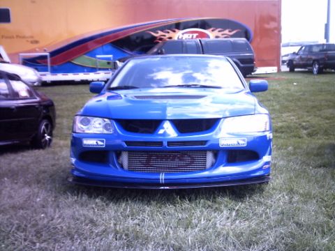1995 Ford Probe - A blue Mitsubishi Lancer Evolution is seen from the front, parked on grass with a large trailer in the background.