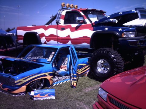 1995 Ford Probe - Customized trucks and a car are displayed outdoors at an event.