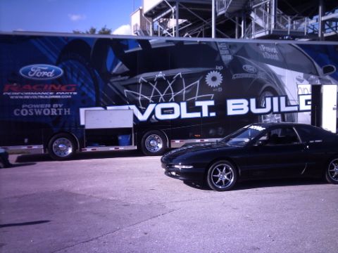 1995 Ford Probe - A black 1995 Ford Probe is parked in front of a large trailer at an outdoor event.