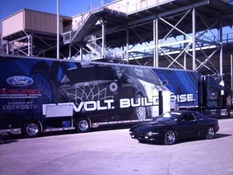 1995 Ford Probe - A black 1995 Ford Probe is parked in front of a large trailer Ford branding and racing graphics.